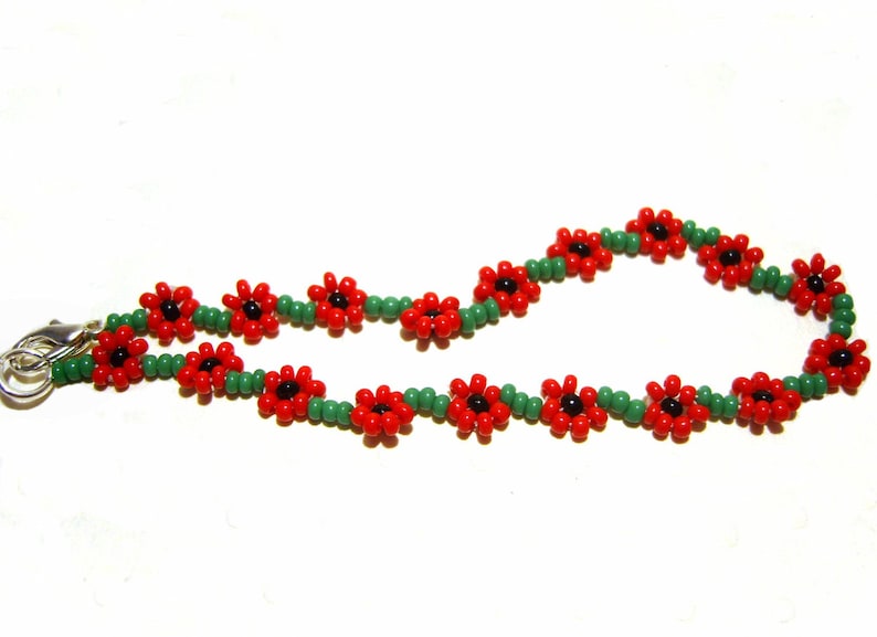 May include: A beaded bracelet with red flower-shaped beads and green spacer beads. The bracelet has a silver clasp.