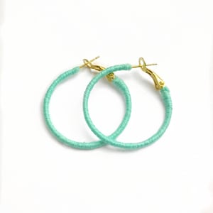 May include: A pair of turquoise hoop earrings with gold-toned clasps. The earrings are made of a thin, woven material.