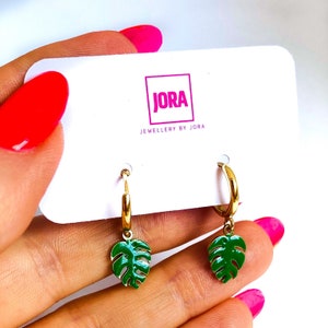 May include: Gold hoop earrings with green monstera leaf charms. The earrings are displayed on a white card with the text "JORA JEWELLERY BY JORA".