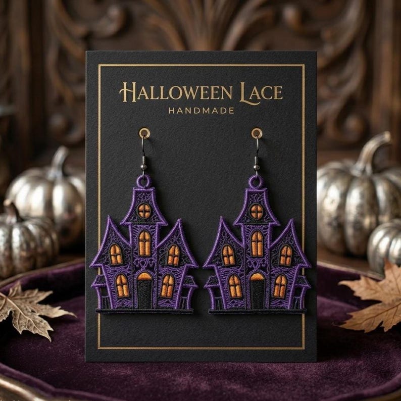 Puede incluir: Un par de pendientes colgantes con forma de casas encantadas, hechos de encaje morado y negro con ventanas naranjas. Los pendientes se presentan en una tarjeta negra con el texto HALLOWEEN LACE HANDMADE en letras doradas.