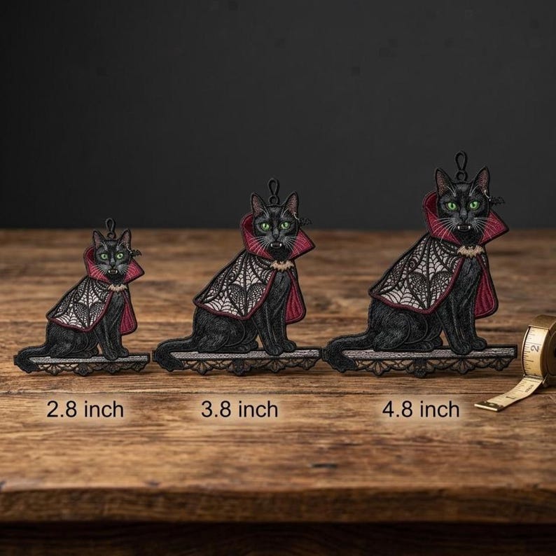 May include: Three black cat embroidered ornaments with green eyes and fangs, wearing red and white spiderweb capes. The ornaments are labeled 2.8 inch, 3.8 inch, and 4.8 inch, with a measuring tape visible next to the largest cat.