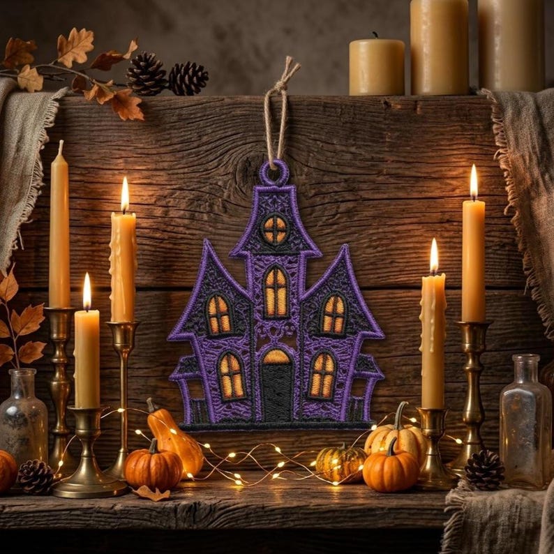 Puede incluir: Un adorno de casa encantada bordado en morado y negro con un lazo de cuerda de yute para colgar. El dise&ntilde;o presenta costuras intrincadas, m&uacute;ltiples techos puntiagudos y ventanas iluminadas en amarillo sobre un fondo de madera r&uacute;stica.