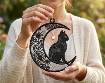 May include: A black embroidered crescent moon ornament featuring a seated black cat with green eyes. The moon is decorated with intricate swirling patterns and silver star motifs. The piece is circular in shape and includes a small loop at the top for hanging, showcasing detailed needlework and contrasting silver thread accents.