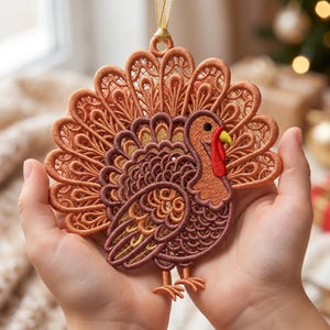 May include: A turkey-shaped hanging ornament crafted from intricate brown and copper-toned embroidery thread. The design features a detailed fanned tail, a red wattle, a yellow beak, and a small loop at the top with a thin gold ribbon for hanging.