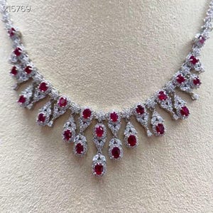 Op de afbeelding: Een zilverkleurige ketting met talrijke ovaal geslepen, dieprode edelstenen en kleinere, heldere stenen. De ketting heeft een delicaat, sierlijk ontwerp met een symmetrische rangschikking van de edelstenen. De tekst "215769" is zichtbaar.