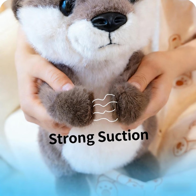 Puede incluir: Un juguete de peluche de nutria con vientre blanco y pelaje gris. El juguete tiene una nariz negra y ojos azules. El texto "Strong Suction" se muestra en el juguete.