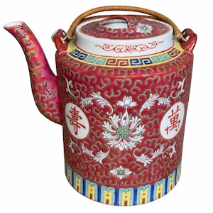 May include: A cylindrical ceramic teapot featuring a vibrant red background with intricate gold scrollwork, white floral motifs, and two circular medallions containing red Chinese characters. It has a curved spout and a woven rattan handle.