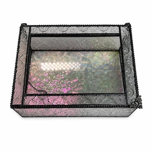 May include: A rectangular glass display box featuring clear, textured glass panels with an embossed floral pattern. The box is framed with dark, metallic soldered edges and includes a hinged lid with a small black chain attached to the interior.