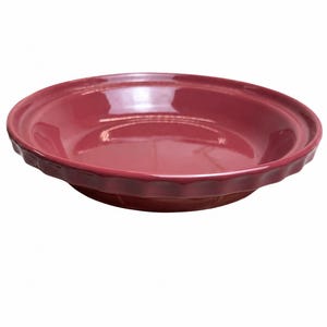 May include: A deep, circular pie dish with a glossy, dark berry-red finish. The dish features a wide, flat rim with a decorative, scalloped edge design that runs along the entire circumference, providing a textured border to the smooth interior.