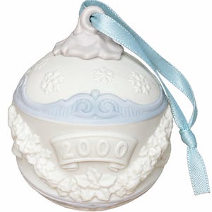 May include: A spherical white ornament featuring embossed snowflake patterns, a central banner with the year 2000, and a decorative floral wreath motif. The ornament is topped with a light blue satin ribbon loop for hanging purposes.