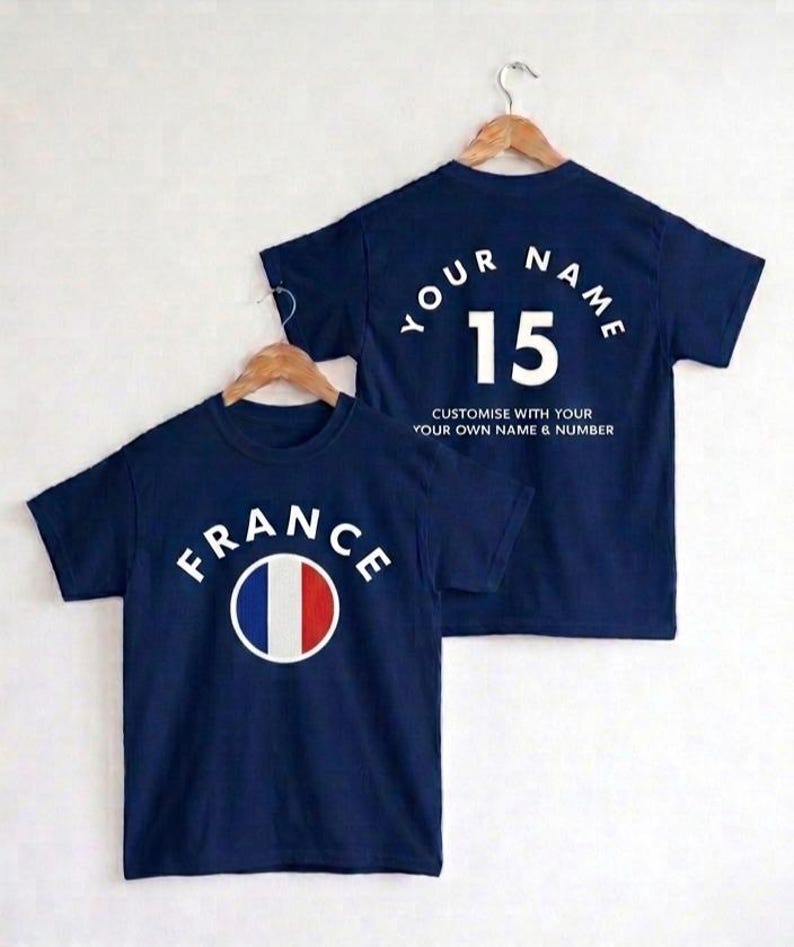 May include: Navy blue t-shirts with the word "FRANCE" and the French flag on the front. The back of one shirt says "YOUR NAME" and "15". The text "CUSTOMISE WITH YOUR OWN NAME & NUMBER" is also on the back.