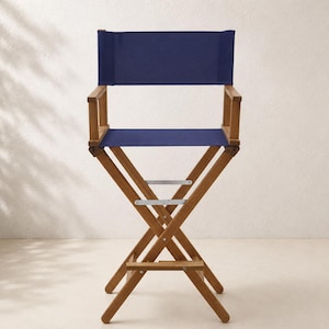Peut inclure: Une chaise de metteur en scène pliante avec une structure en bois naturel et une assise ainsi qu'un dossier en tissu bleu marine uni. La chaise comprend deux accoudoirs, un repose-pieds et des fixations métalliques argentées.
