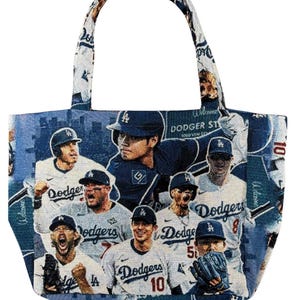 May include: A tote bag featuring a woven tapestry design of Los Angeles Dodgers baseball players in white and blue uniforms. The fabric displays multiple player portraits, the Dodgers team logo, and the text Dodger Stadium in a repeating pattern.