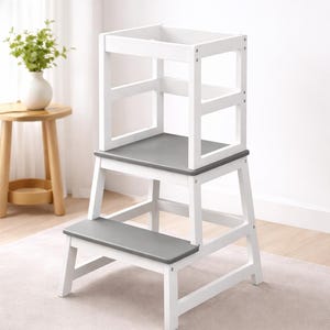 May include: A white wooden step stool with a gray platform and step. The step stool has a square top section with side rails. The design is simple and modern, suitable for various home settings.