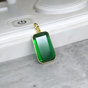 May include: A rectangular green pendant with a gold-colored frame. The pendant has a gradient effect, transitioning from a darker green at the top to a lighter green at the bottom. The pendant is suspended from a gold-colored bail.