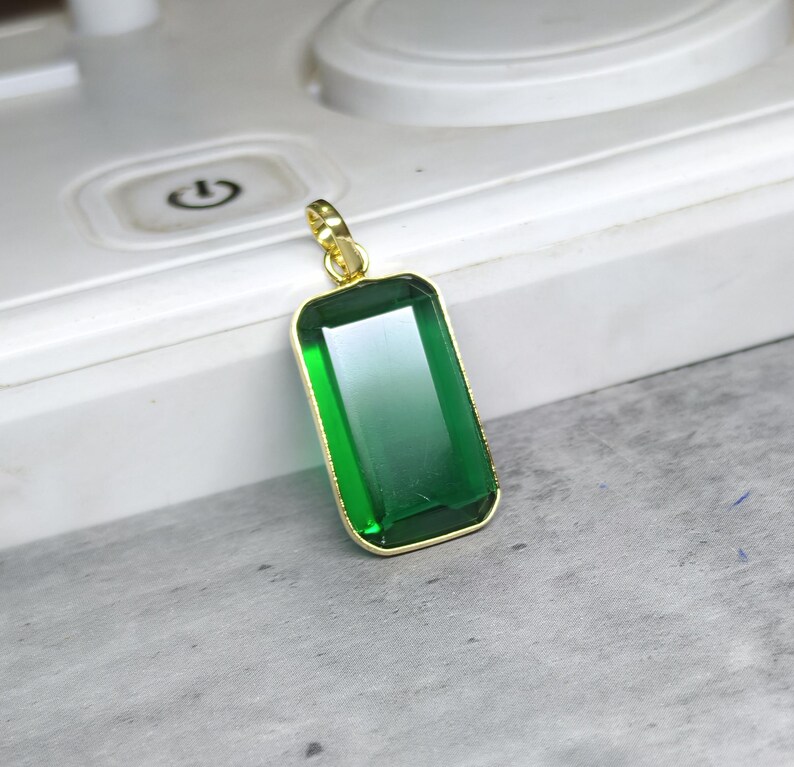 May include: A rectangular green pendant with a gold-colored frame. The pendant has a gradient effect, transitioning from a darker green at the top to a lighter green at the bottom. The pendant is suspended from a gold-colored bail.
