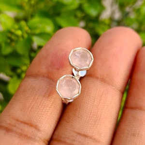 Op de afbeelding: Een paar oorknopjes met ronde, lichtroze gefacetteerde edelstenen in zilverkleurige metalen zettingen. Elke oorbel heeft een gladde, gepolijste rand rondom de steen, wat zorgt voor een eenvoudig en strak ontwerp voor dagelijks gebruik.