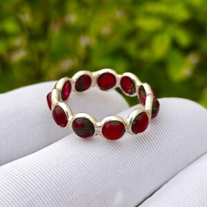 Pode incluir: Um anel de banda de prata com uma fila contínua de pedras cabochão circulares em engaste de bisel. Cada pedra apresenta uma cor vermelha profunda com subtis inclusões manchadas de verde escuro e castanho nas superfícies polidas e arredondadas.