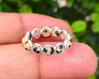 May include: A silver ring featuring a series of round, speckled beige stones. The stones have black spots, resembling a dalmatian's coat. The ring is set in a silver band, creating a simple yet elegant design. The ring is a piece of jewelry.