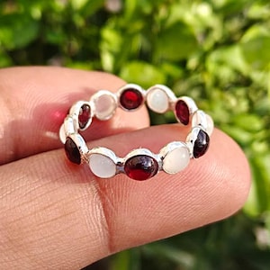 Könnte beinhalten: Ein silberner Ring mit abwechselnd roten und weißen Edelsteinen. Der Ring hat ein durchgehendes Band aus rund geschliffenen Steinen. Die Edelsteine sind in einem silbernen Band gefasst und erzeugen einen klassischen und eleganten Look.