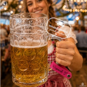 Könnte beinhalten: Ein großer, klarer Bierkrug aus Glas mit genoppter Struktur, gefüllt mit goldenem Bier und weißem Schaum. Am Henkel ist ein leuchtend pinkes Lederband befestigt, das den schwarzen Schriftzug "Wiesnmadl" und ein kleines Herzsymbol trägt.