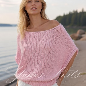 Può includere: Un maglione in maglia rosa chiaro, dalla vestibilità ampia e maniche corte, con un ampio scollo a barchetta e un orlo a coste. Il capo presenta un motivo a maglia aperta e testurizzata. Il testo "Yanas Knits" è sovrapposto in bianco in basso.