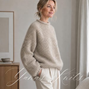 Könnte beinhalten: Ein beigefarbener, langärmeliger Strickpullover mit Rundhalsausschnitt und lockerer Passform. Das Kleidungsstück besteht aus strukturiertem, flauschigem Garn mit gerippten Details an den Ärmelbündchen und am Kragen, kombiniert mit einer hellen Hose.