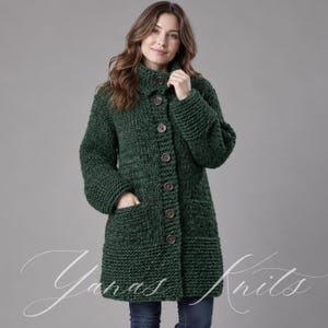May include: A dark forest green chunky knit cardigan featuring a high collar, long sleeves, and a front button closure with six large brown buttons. The garment includes two front patch pockets and is labeled with the text Yanas Knits.