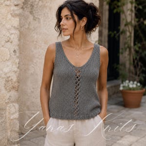 Può includere: Un top senza maniche grigio lavorato a maglia con scollo a V e un design a griglia centrale. Il top è senza maniche e ha una vestibilità rilassata. Il testo "Yanas Knits" è visibile nell'angolo in basso a sinistra. La modella indossa pantaloncini beige.