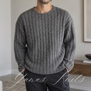 May include: A charcoal grey long-sleeve jumper featuring a vertical ribbed knit pattern, a crew neckline, and cuffed sleeves. The garment is worn with plain black trousers. The text Yanas Knits is overlaid in white script across the lower portion.