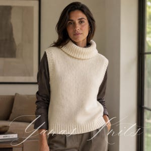 May include: A cream-colored sleeveless knit sweater vest featuring a thick ribbed turtleneck collar, a vertical ribbed knit pattern throughout the body, and a wide ribbed hemline, worn over a dark brown long-sleeved shirt and dark trousers.