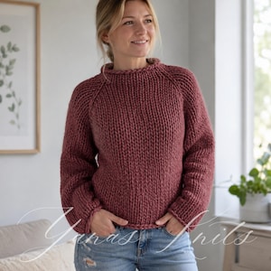 Può includere: Un maglione a maglia grossa color rosa polvere con scollo rotondo, maniche lunghe con polsini a coste e un dettaglio a bordo intrecciato spesso lungo il colletto e l'orlo. Il capo presenta una lavorazione a maglia pesante e strutturata.