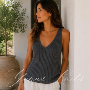 May include: A dark charcoal gray sleeveless tank top featuring a deep V-neckline and a vertical ribbed knit texture. The garment is constructed with wide shoulder straps and a straight hemline, providing a fitted silhouette throughout the torso.