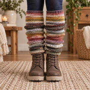 May include: A pair of multi-coloured, hand-knitted leg warmers featuring horizontal stripes in shades of mustard yellow, deep red, forest green, white, and brown. The leg warmers are worn over dark blue denim jeans and paired with brown lace-up boots.