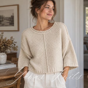 May include: A beige knit jumper featuring a round neckline, three-quarter length sleeves, and a vertical seam detail down the centre front. The garment has a ribbed hem and ribbed sleeve cuffs, crafted from a textured, light-coloured yarn material.