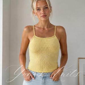 Può includere: Un top a canotta in maglia giallo pallido con scollo quadrato e sottili spalline. Il capo è realizzato con una texture a coste verticali ed è abbinato a jeans azzurri. Il design complessivo è semplice e senza maniche.