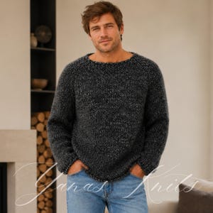 May include: A chunky knit sweater in a dark charcoal and black marled yarn with a round neckline and long sleeves. The sweater features a thick, textured stitch pattern and a relaxed fit, paired with light blue denim jeans with visible pockets.