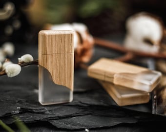 May include: A rectangular lighter with a wooden top and a clear, transparent bottom. The lighter is made of wood and clear plastic. The lighter is sitting on a dark, textured surface. Two additional lighters are in the background.