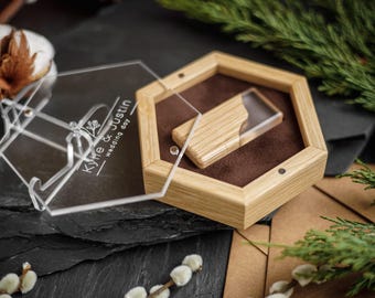 Puede incluir: Una caja hexagonal de madera con interior de terciopelo marrón oscuro que contiene una memoria USB de madera a juego. La caja tiene una tapa de acrílico transparente grabada con el texto "Kyle & Justin wedding day" y un diseño floral.
