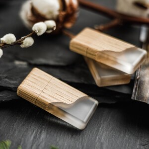 May include: Two rectangular USB flash drives featuring a combination of light-toned wood and a translucent, frosted resin section with a wavy edge. The drives have a smooth, natural wood grain finish and a sleek, modern design.