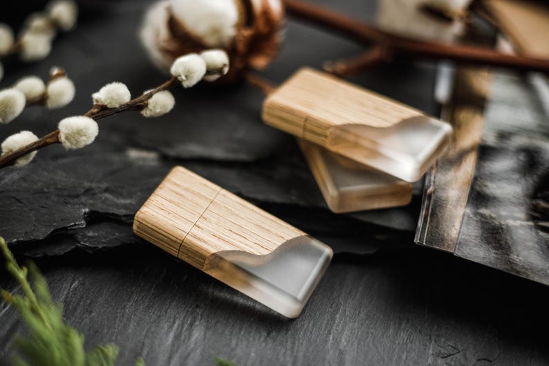 May include: Two rectangular USB flash drives featuring a combination of light-toned wood and a translucent, frosted resin section with a wavy edge. The drives have a smooth, natural wood grain finish and a sleek, modern design.