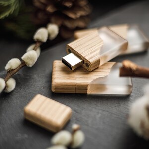 May include: A set of USB flash drives featuring a combination of light-toned wood and clear, translucent resin. The drives have a rectangular shape with a metallic silver connector exposed on one end, showcasing a natural wood grain texture.