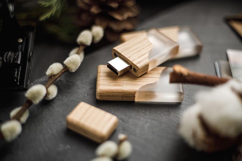 May include: A set of USB flash drives featuring a combination of light-toned wood and clear, translucent resin. The drives have a rectangular shape with a metallic silver connector exposed on one end, showcasing a natural wood grain texture.