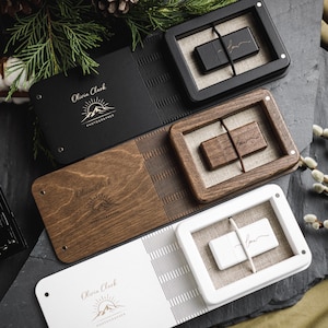 May include: A selection of wooden and black USB drive boxes and photo albums, some with the name "Olivia Clark Photographer" and a mountain logo. The USB drives are displayed in wooden frames with a linen backing.