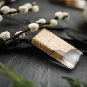 May include: A wooden lighter with a clear resin end sits on a dark, textured surface. The lighter is made of light-coloured wood and has a rectangular shape. Pussy willow branches with white buds are in the background.