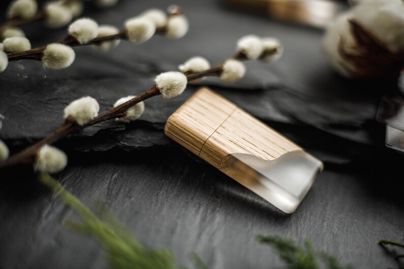 May include: A wooden lighter with a clear resin end sits on a dark, textured surface. The lighter is made of light-coloured wood and has a rectangular shape. Pussy willow branches with white buds are in the background.