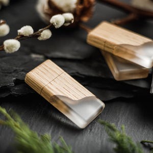 May include: Two rectangular USB flash drives featuring a combination of light brown wood grain and a translucent, frosted white resin section. The drives have a smooth, flat surface and a distinct seam where the wood meets the resin material.