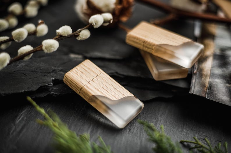 May include: Two rectangular USB flash drives featuring a combination of light brown wood grain and a translucent, frosted white resin section. The drives have a smooth, flat surface and a distinct seam where the wood meets the resin material.