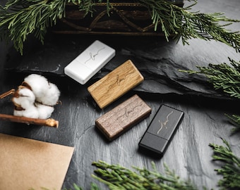 May include: Four USB flash drives in white, light wood, dark wood, and black. Each drive has the word "love" in a cursive font. The drives are arranged on a dark, textured surface with sprigs of greenery and a cotton boll.