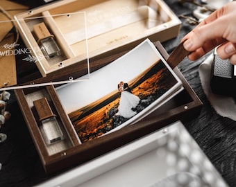 Puede incluir: Cajas de fotos de madera con tapa de acrílico transparente y una unidad USB. Las cajas contienen fotos de boda. La imagen muestra a una persona abriendo la caja para revelar las fotos. Las cajas están sobre una superficie de madera oscura.